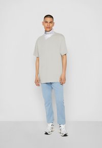 Tricou gri din bumbac cu mâneci scurte, asortat cu pantaloni de culoare bleu deschis. O bandană albă cu accente negre este purtată în jurul gâtului.