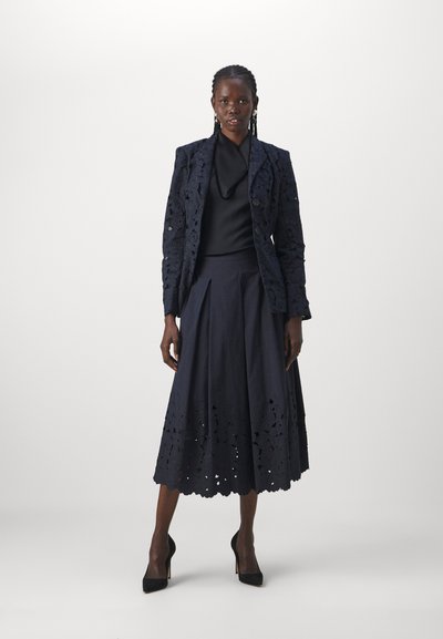 Navy lace blazer with floral cutouts, paired with a plain black top and a matching midi skirt featuring a similar lace hem. Black high heels.