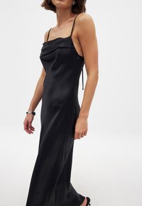 Black satin slip dress with a cowl neck design, thin straps, and a form-fitting silhouette, featuring a smooth, glossy texture.