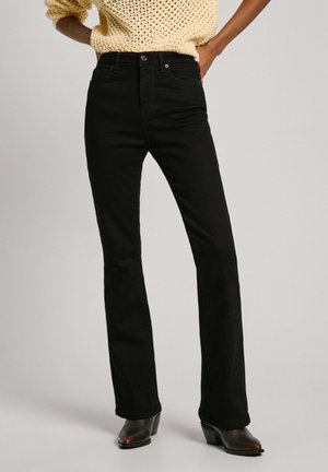 Jean évasé noir en denim, avec une taille haute, des poches avant et une simple fermeture par bouton, associé à un pull en tricot crème.