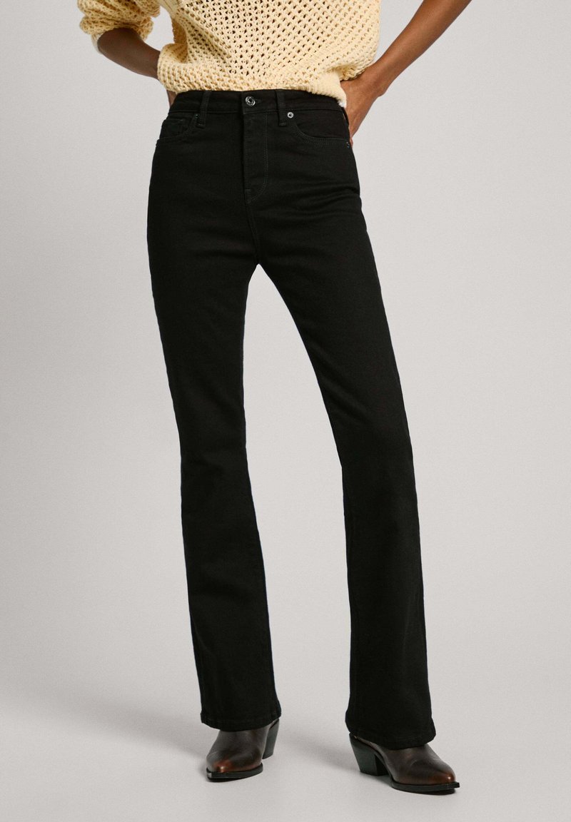 Jeans de campana negros hechos de mezclilla, con cintura alta, bolsillos frontales y cierre de botón sencillo, combinados con un suéter de punto crema.