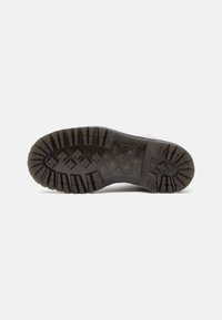 Suela de goma negra con profundas estrías y pequeños patrones. Áreas del dedo del pie y del talón reforzadas, que proporcionan tracción y durabilidad.