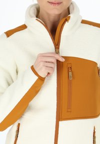 Fleece jacket with cream body and orange accents. Features a full zipper, a zippered chest pocket, and contrasting sleeve materials.