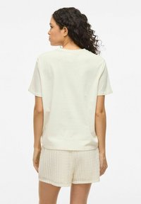 Camiseta de algodón en color beige claro con mangas cortas, combinada con pantalones cortos blancos texturizados con un patrón tejido, vista desde la parte posterior.