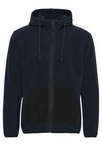Chaqueta con capucha de forro polar azul marino que presenta un bolsillo frontal negro, cierre de cremallera y cordones con acentos verdes en la capucha. Textura suave.