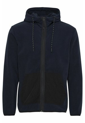 Granatowa polarowa kurtka z kapturem z czarną kieszenią z przodu, z zamkiem błyskawicznym oraz sznurkami z zielonymi akcentami na kapturze. Miękka faktura.