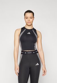 Crop top de sport noir avec des accents gris et un col montant, arborant un logo blanc. Associé à des leggings noirs taille haute portant une marque.