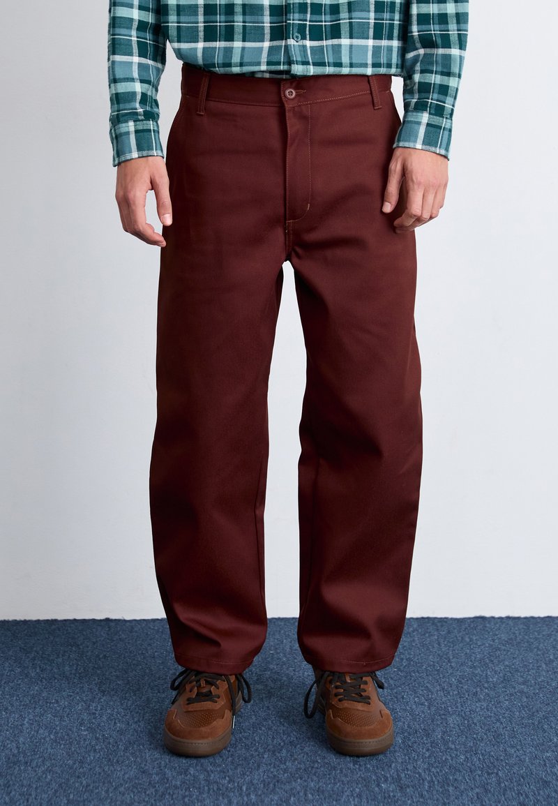 Maroon wide-leg pants with a sturdy fabric and front pockets. Paired with brown multi-textured shoes and a plaid green shirt.
