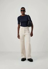 Navy fitted t-shirt, cream wide-leg pants, and black platform shoes. Accessories include sunglasses and a black handbag. Smooth fabric and tailored fit.