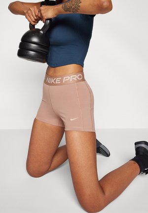 Personne en short Nike Pro rose et haut bleu marine agenouillée, tenant un kettlebell noir au niveau de la poitrine.