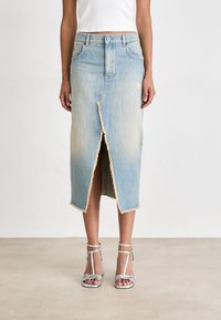 Fustă midi din denim albastru deschis, cu o despicătură în față, tiv brut și margini desfăcute. Purta sandale argintii cu bretele.