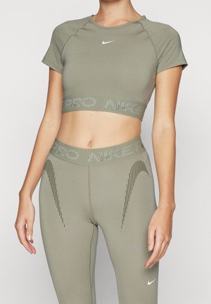 Kobieta nosząca oliwkowo zielony sportowy krótki top Nike Pro i dopasowane legginsy z wysokim stanem z subtelnymi logo Swoosh i teksturowanymi paskami.