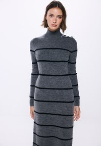 Abito a maglia grigio con strisce orizzontali nere, collo alto, maniche lunghe e dettaglio a bottoni sulla spalla. Tessuto morbido e con texture.