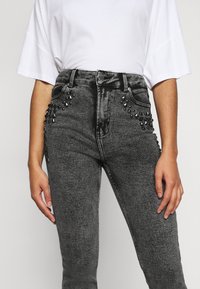 Högmidjade svarta sten-tvättade jeans med silverfärgade nitar på framfickorna och en klassisk femfickorsdesign.