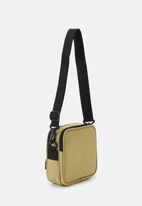 Żółta prostokątna torba na ramię z czarnym paskiem i zamkami błyskawicznymi, wykonana z trwałej tkaniny, wyposażona w boczną kieszeń i fakturowaną powierzchnię.