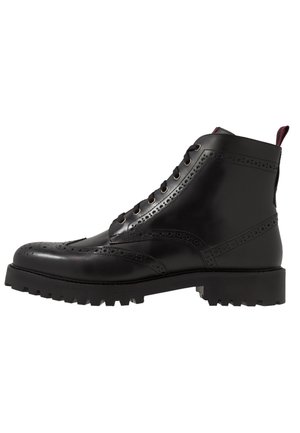 Mustat nahkaiset brogue-nauhakengät paksulla pohjalla ja koristeellisilla rei'ityksillä, nähtynä ulkosivulta.