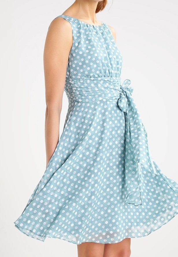 Ein hellblaues Kleid mit weißen Punkten, ärmelloses Design, Taillenknoten und schwingendem Rock. Hergestellt aus einem leichten, strukturierten Stoff.