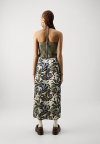 Grön smockat liv med halterneck, parat med en lång kjol med ett djärvt blommönster i blå, lila och gräddtoner.