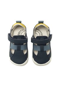 Sandalias de cuero azul marino con diseño abierto, tira ajustable, costuras expuestas y un interior claro. Presentan un acento amarillo en el talón.