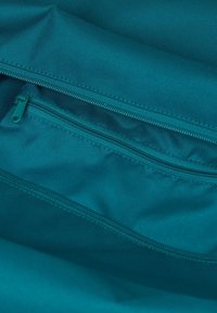 Türkise Stofftasche mit glatter Textur, ausgestattet mit zwei Reißverschlusstaschen, die durch kontrastierende Nähte umrissen sind.