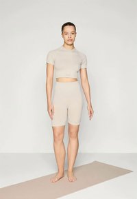 Bežs sporta apģērba komplekts, kas sastāv no īsām piedurknēm un īsām biksēm ar augstu jostas vietu, izgatavots no gludas, elastīgas auduma.