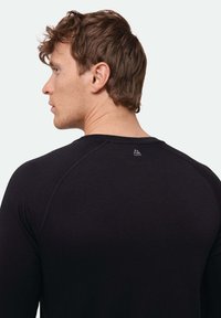 Schwarzes Langarmshirt mit strukturierter Oberfläche, Raglanärmeln und einem kleinen Logodetail nahe dem Nacken auf der Rückseite.