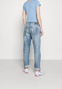 Ljusblå denimjeans med en avslappnad passform, med uppvikt fåll och slitet utseende. Kombinerad med en ljusblå skjorta och vita sneakers.