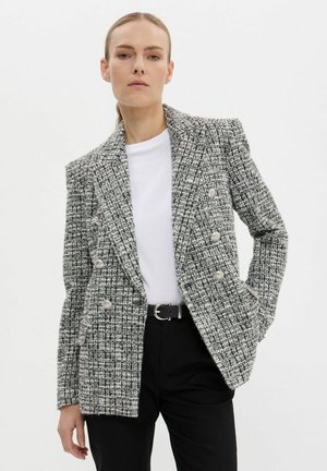 Gray and white tweed blazer with a double-breasted design, metallic buttons, and a textured finish. Worn over a white shirt and black pants.