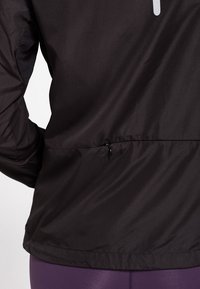 Czarna lekka kurtka z taliowanym pasem ze ściągaczem. Materiał wydaje się gładki i wytrzymały, odpowiedni do noszenia na zewnątrz.