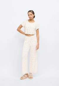 Σετ πυτζάμας σε ανοιχτό μπεζ χρώμα με κοντό τοπ με κυματιστές άκρες και σχέδια ροζ καρδιών, συνδυασμένο με παντελόνια φαρδιάς γραμμής. Ζεστά παντόφλες από απαλό βελούδο.