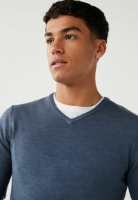 Dunkelblauer V-Ausschnitt-Pullover aus Strickstoff. Verfügt über ein tailliertes Design und einen Lagenlook mit einem weißen Rundhalsausschnitt-T-Shirt darunter.