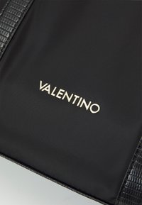 Svart nylonväska med texturerade svarta lädersidor. Har "Valentino"-logotypen i guld. Slät yta med subtil glans och kraftig sömnad.