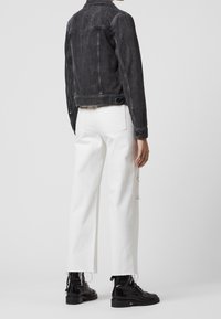 Černá džínová bunda s přiléhavým střihem, v kombinaci s bílými džíny s oprýskaným vzhledem a třásněmi na lemech, a černými šněrovacími botami.