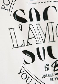Close-up of white fabric with black text and dotted design, featuring the phrase "I AM SOUL" and additional decorative lettering.