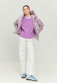 Lilac puffer jacket with hood, paired with a purple knit sweater, white wide-leg pants, and blue sneakers with white stripes.