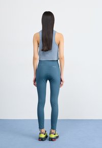 Avskåret blå tanktopp, tealfargede leggings og joggesko med gule detaljer; glatt, elastisk stoff og tettsittende design.