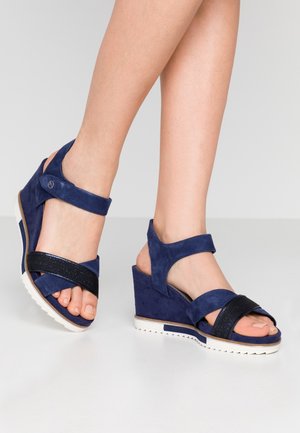 Sandales à talons compensés en suède bleu marine avec des sangles réglables et une bande d'accent texturée noire. Présente une semelle blanche avec un motif en relief pour une meilleure adhérence.