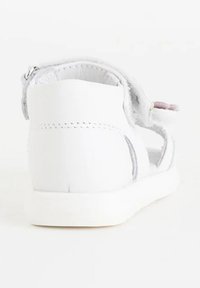 Sandal bianca con una texture morbida, chiusura con zip sul retro e una suola piatta e bianca. Design aperto con dettagli di cucitura minimi.