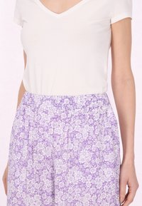 Witte korte mouw v-hals shirt gecombineerd met paarse, bloemenpatroon, elastische taillebroek met overal kleine witte bloemen.