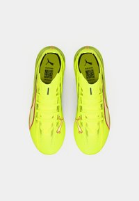 Los tacos de fútbol amarillos brillantes cuentan con una parte superior texturizada, cordones, una línea de acento roja y un pequeño logo de Puma en el lateral.