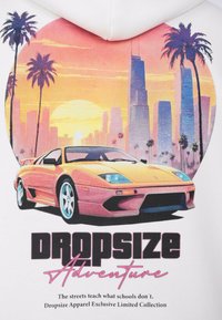 Gul bil foran en solnedgang over byens skyline med palmer, over teksten "Dropsize Adventure" på en hvid baggrund.