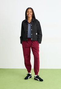 Sort letvægtsjakke med to forlommer, båret over en blå tekstureret mesh-skjorte. Burgundy sweatpants med elastiske manchetter og sorte sneakers.