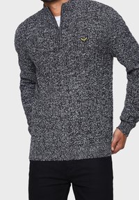 Schwarz-weißer gestrickter Pullover mit einem Reißverschlusshals, der einen strukturierten Stoff und ein kleines Logo auf der Brust besitzt.