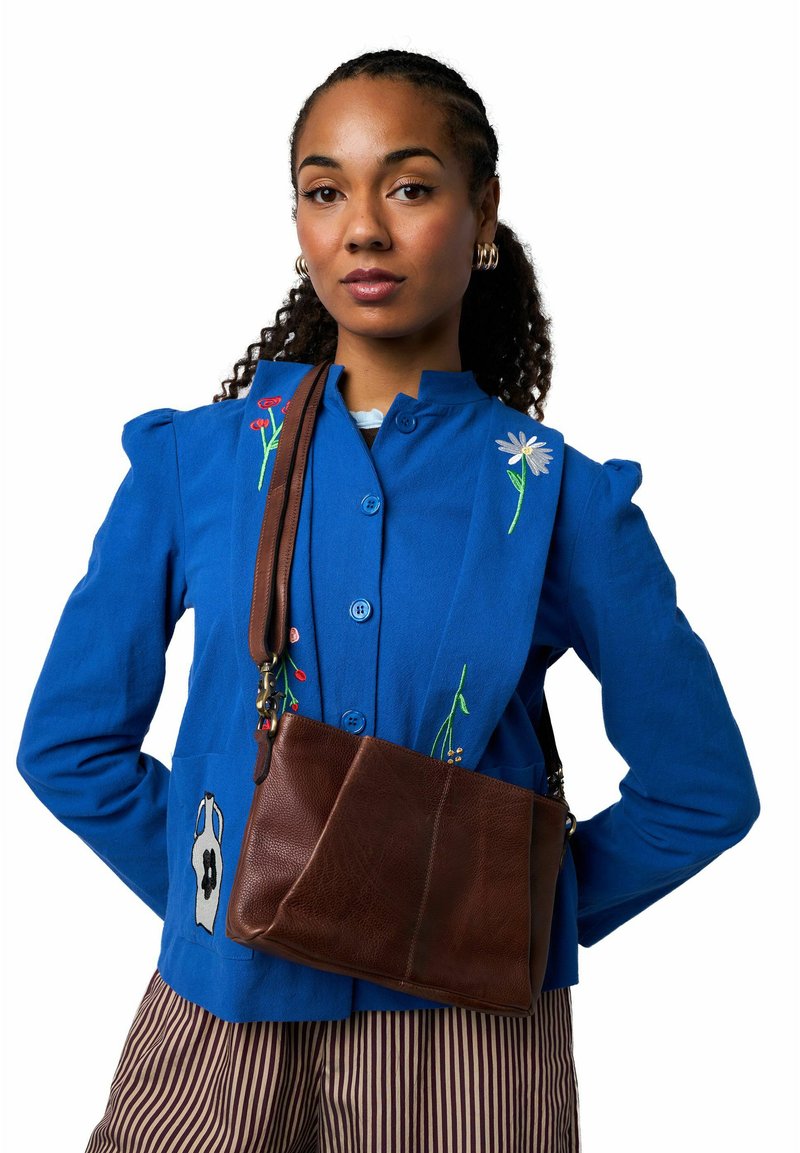 Veste bleue boutonnée avec broderie florale et sac bandoulière en cuir marron. Pantalon rayé avec un design simple et légèrement brillant.
