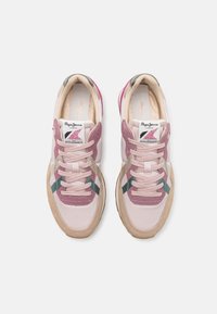 Baskets rose clair avec des accents en suède mauve, dotées d'une bande verte et d'une semelle en caoutchouc beige texturée. Les lacets sont d'un rose pâle.