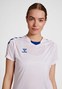 Camiseta atlética blanca con acentos azules. Presenta un cuello redondo, mangas cortas y un logo en el pecho. Fabricada con tejido suave y ligero.