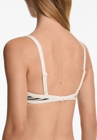Beige bh med tunna band, med svarta detaljer och justerbara spännen på baksidan. Slät yta med en figurnära design.