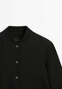 Veste bomber noire avec col côtelé, boutons-pression à l'avant et deux poches avant, vue de la poitrine vers le haut sur fond blanc.