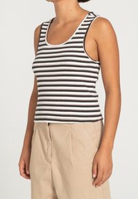 Černobílý pruhovaný top bez rukávů s přiléhavým střihem, úzkými ramínky a žebrovanou texturou, spárovaný s volnými béžovými kalhotami.