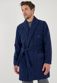 Navyblauer Fleece-Bademantel mit Schalkragen, Bindegürtel und Seitentaschen, mit einem dezenten Logo auf der Brusttasche. Weiche Textur.